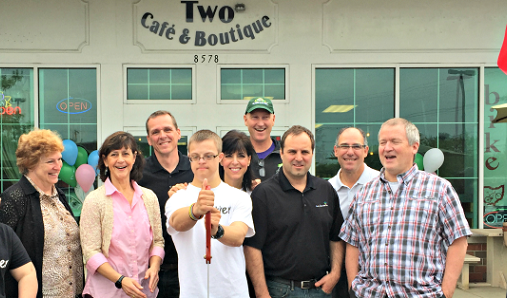 A group of people stand outside storefront for ribbon cutting of Two Cafe and Boutique opening