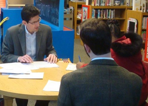 Two men and a girl sit at a library desk during a legal clinic