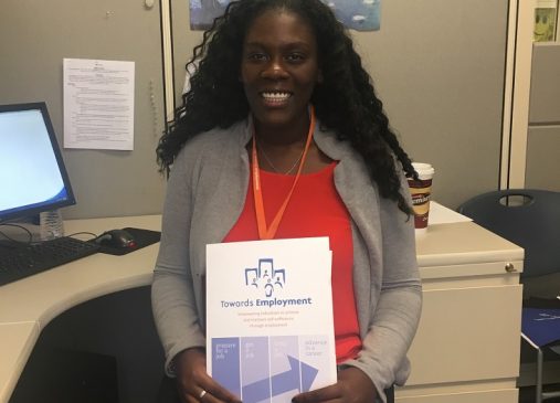 Briana Snoddy sits at her desk holding a Towards Employment document