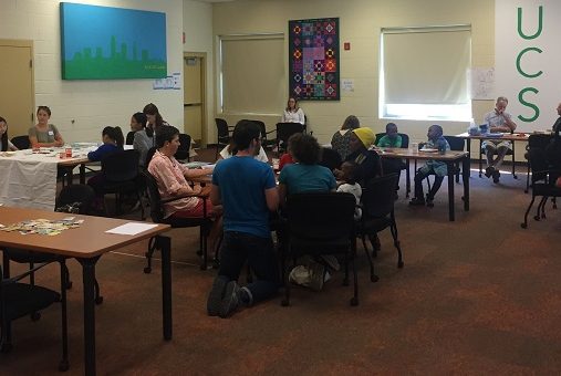 Image of a group of people seated at tables in a room as part of a Refugee Response program.