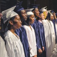 High school graduates stand in a line dressed in their caps and gowns