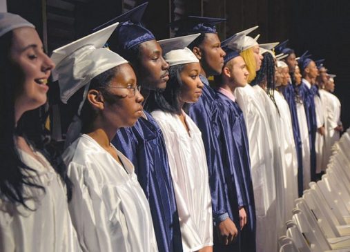 High school graduates stand in a line dressed in their caps and gowns