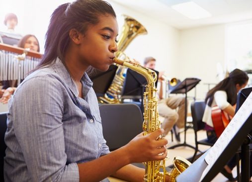 Female Pupil Playing Saxophone In High School Orchestra