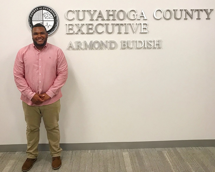 Ricardo stands in front of the Cuyahoga County seal on the wall of the county offices