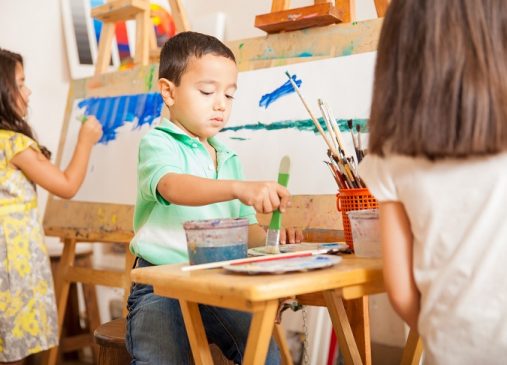 Three kids mixing paint and working on a painting during art class at school