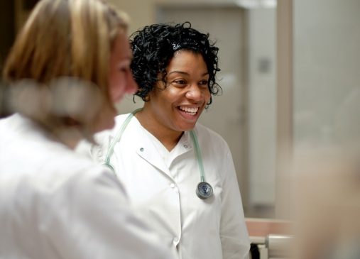 Two nurses stand next to each other in white lab coats