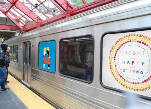 An image of the side of an RTA train at the station platform with windows decorated in colorful art