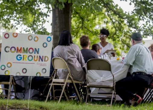 A common ground yard sign is visible in front of a group of people seated at a table outdoors