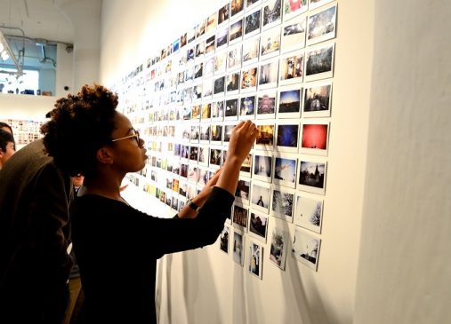 A young girl points to a wall of pictures taken by Cleveland Print Room students