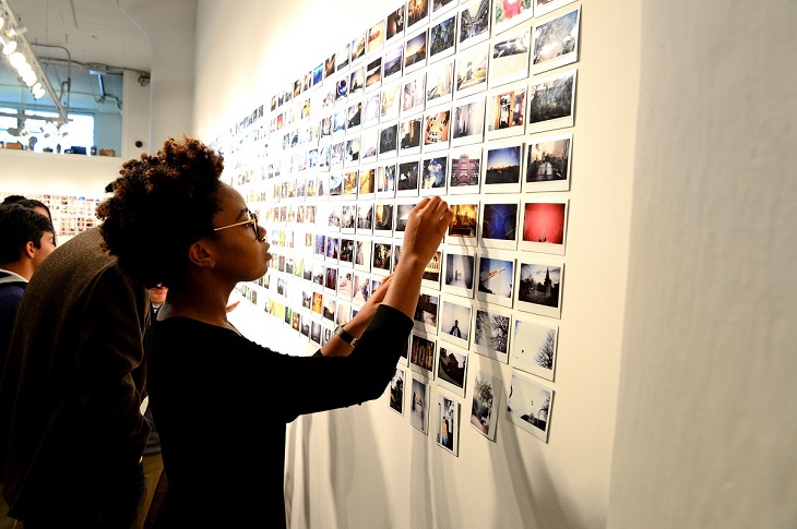 A young girl points to a wall of pictures taken by Cleveland Print Room students