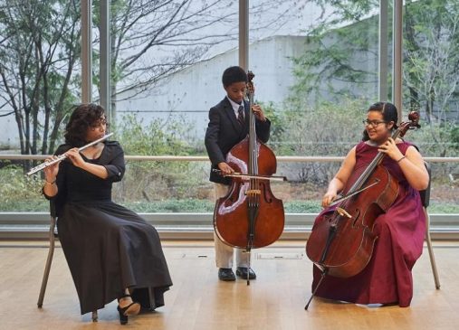 Three students play classical instruments on stage