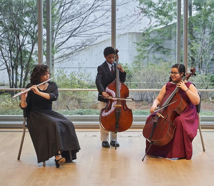 Three students play classical instruments on stage