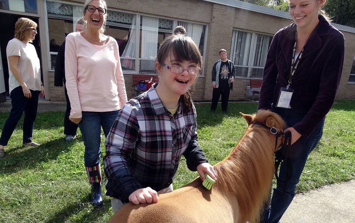 A young girl with Down Syndrom pets a miniature horse 