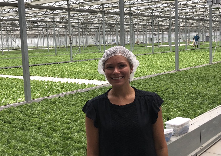 Caroline Carulas stands in front of rows of lettuce inside Evergreen greenhouse