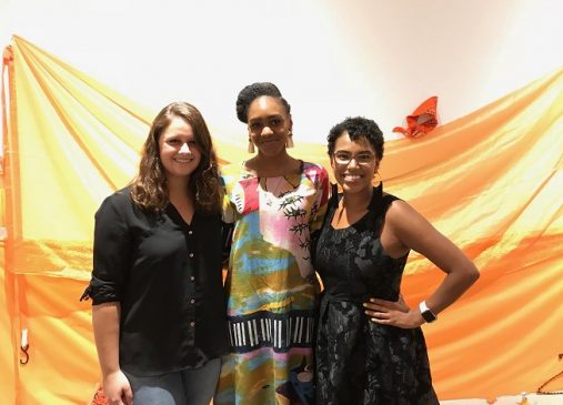 Three women stand in front of orange backdrop