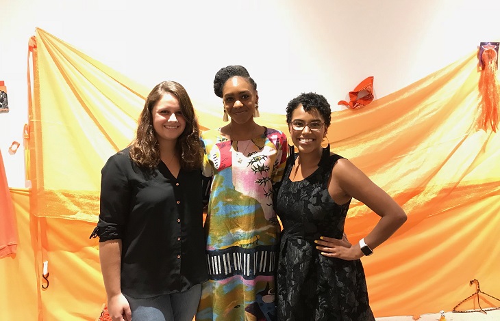 Three women stand in front of orange backdrop