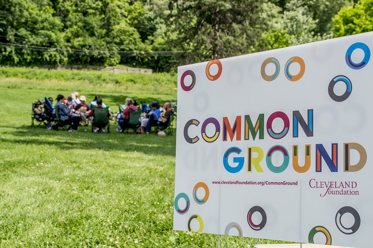 Image of Common Ground yard sign with group of people sitting in distance