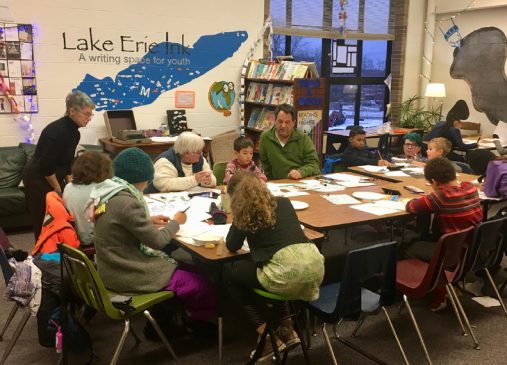 A group of students and instructors sit around a table at Lake Erie Ink