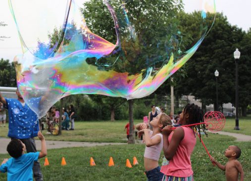 Children play with giant bubble wands in a park