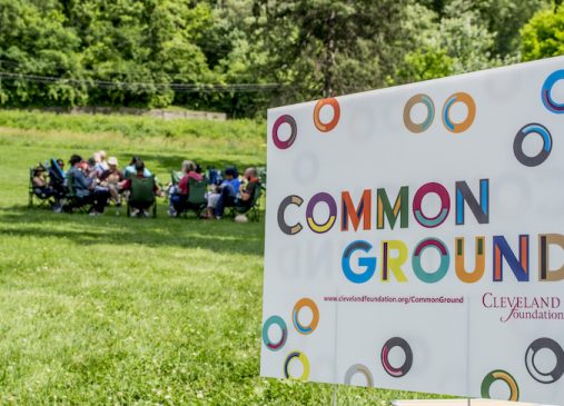 Common Ground yard sign with grassy field and group of people in the background