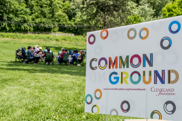 Common Ground yard sign with grassy field and group of people in the background