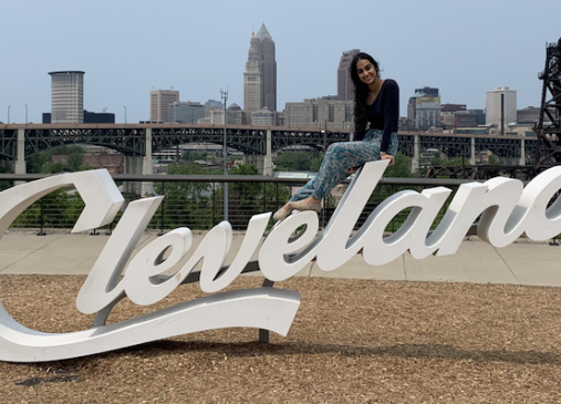 Meshal sitting on top of the Cleveland script sign with city skyline in background