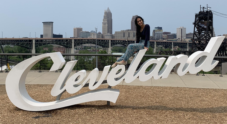 Meshal sitting on top of the Cleveland script sign with city skyline in background