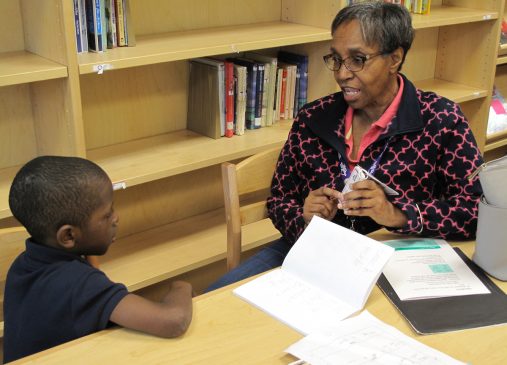 An older adult sits at a table working with a young student
