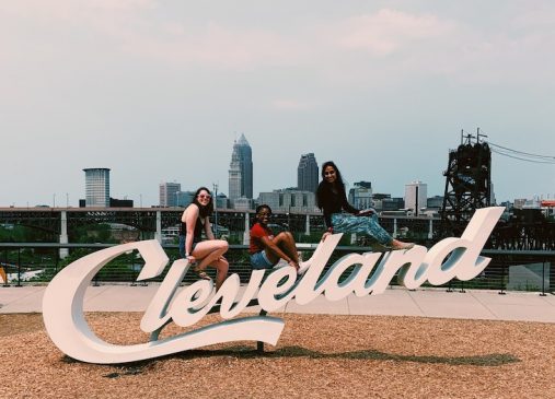 Maggie and other interns pose on the Cleveland script sign with skyline in background