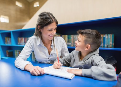 a woman helps a boy with homework at a library desk