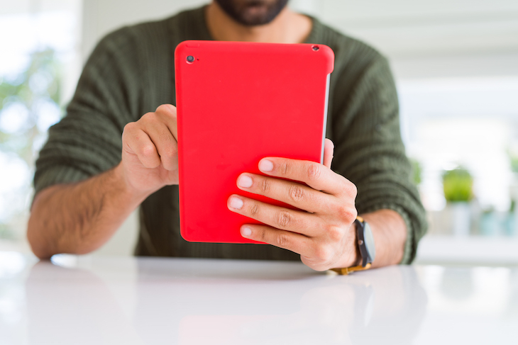 man seated at table holds red ipad