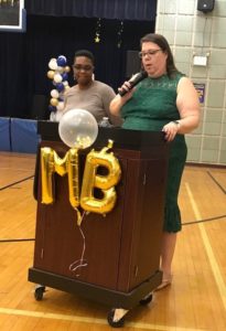 Two women stand at a podium in a school gymnasium