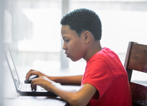 Young teenage boy working on homeschool assignments using laptop at home