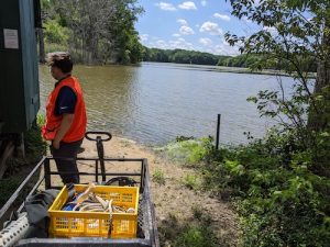 Photo of a man and cart of equipment standing next to a lake 