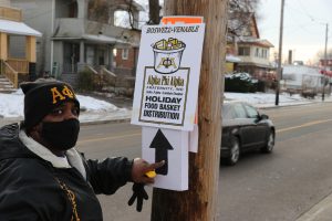 Member of Alpha Phi Alpha fraternity pointing to a holiday food distribution event sign