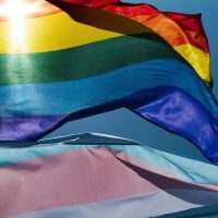 close up of gay pride flag and transgender pride flag against blue sky
