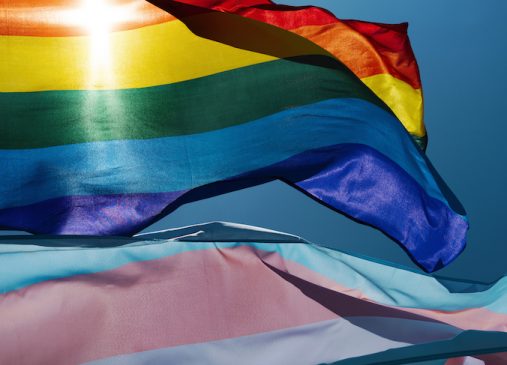 close up of gay pride flag and transgender pride flag against blue sky