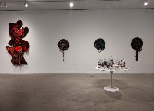 Image of abstract art installation against white gallery wall with table covered in bottles