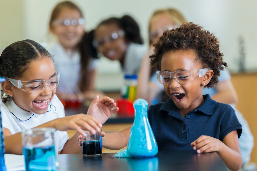 A group of young girls in a science lab sit in front of a beaker doing an experiment