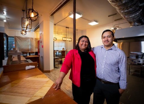 Two people stand inside their restaurant building