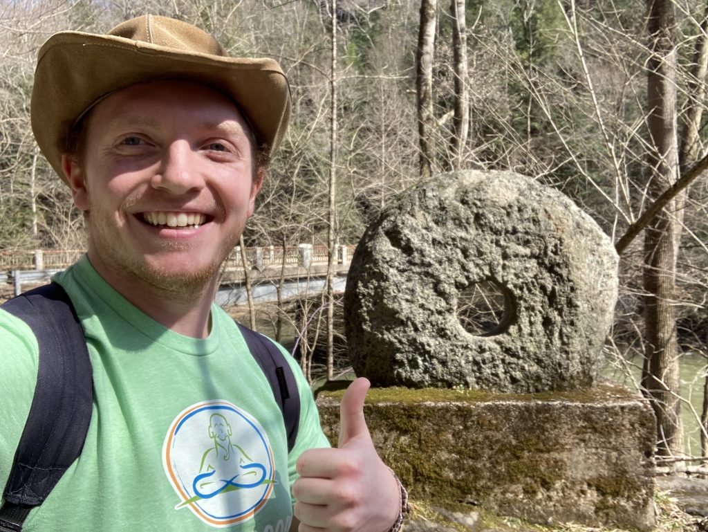 Ale stands outside giving a thumbs up in front of a stone wheel
