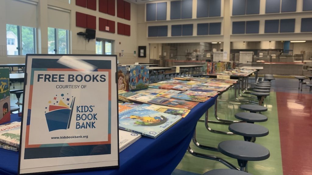 A Cleveland Kids Book Bank sign offers free books laid out on a cafeteria table