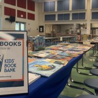 A Cleveland Kids Book Bank sign offers free books laid out on a cafeteria table