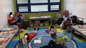 A group of children sitting in chairs and laying on a carpet read books individually