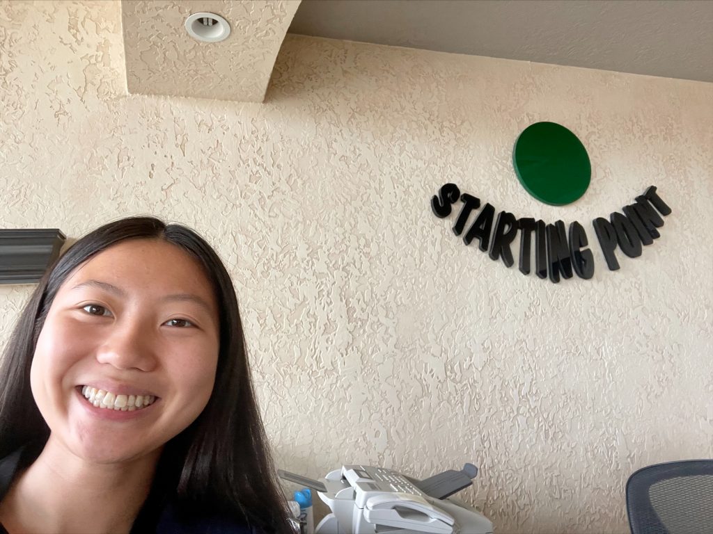 Joy Mason taking a selfie in front of a wall with Starting Point's logo on it