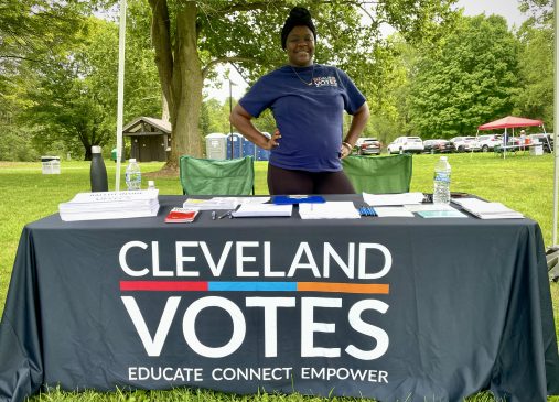 A woman stands behind a Cleveland Votes information table at an outdoor event
