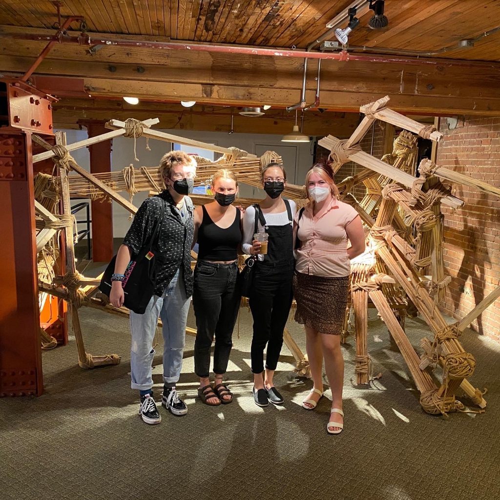 A group of interns stand in front of a wooden sculpture indoors