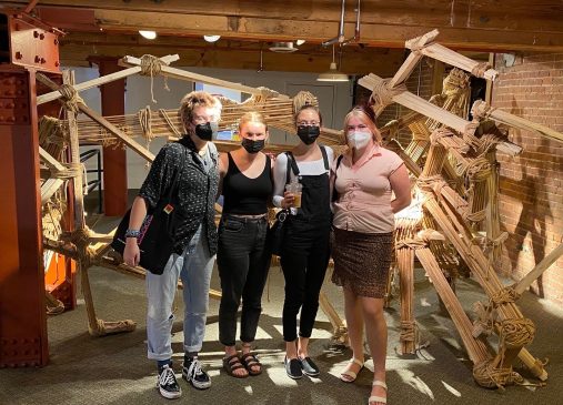 A group of interns stand in front of a wooden sculpture indoors
